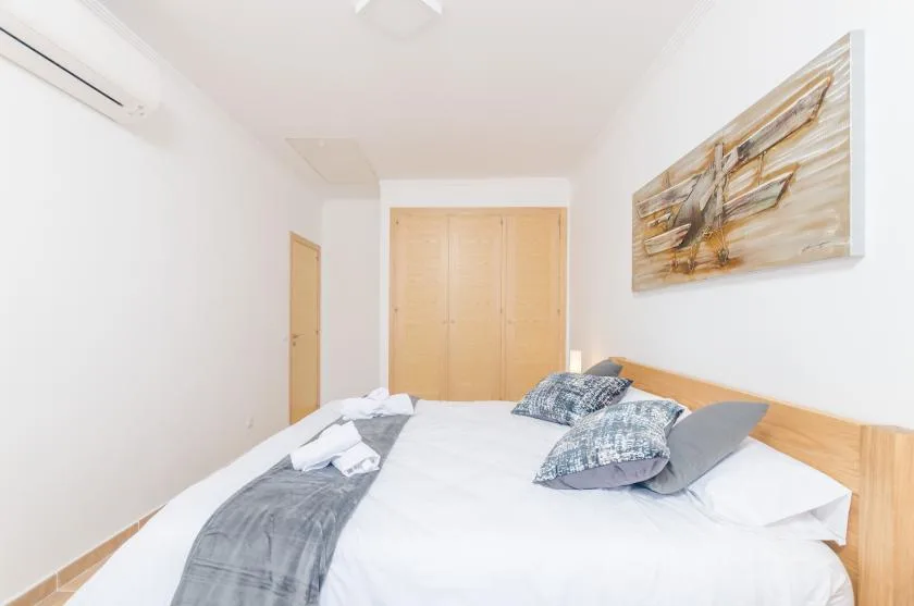 A bright bedroom with a bed, patterned pillows, and wall art.