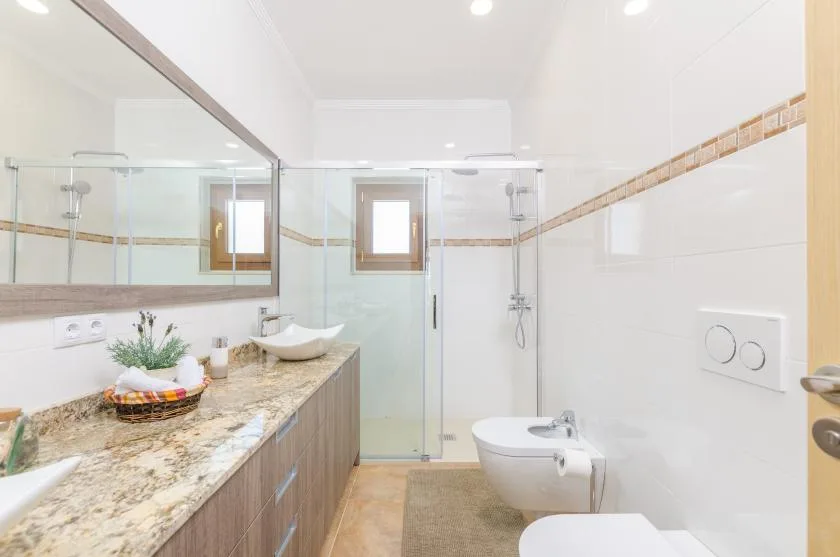 A bright bathroom with a long vanity, a glass shower, and white fixtures.