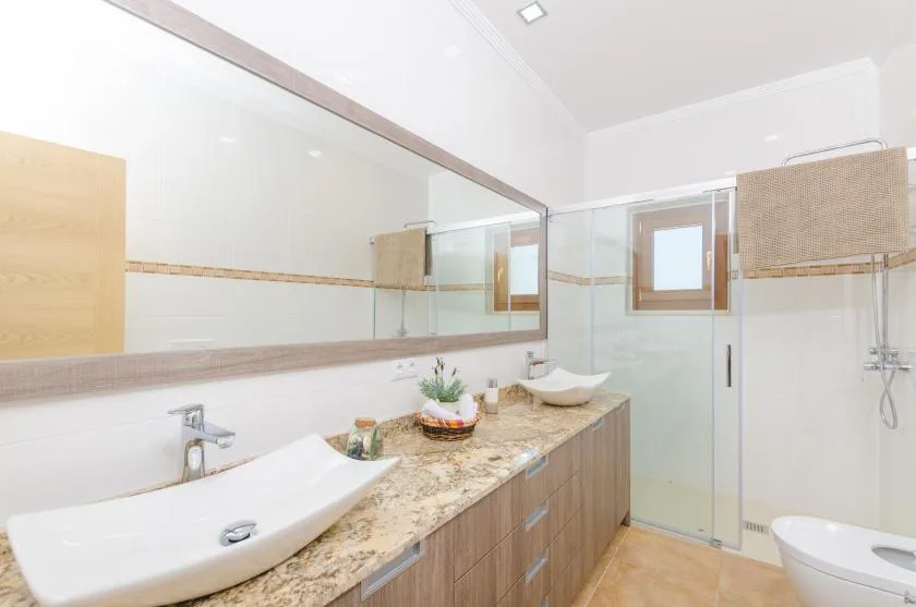 A bright bathroom with a long vanity, vessel sinks, and a glass shower.
