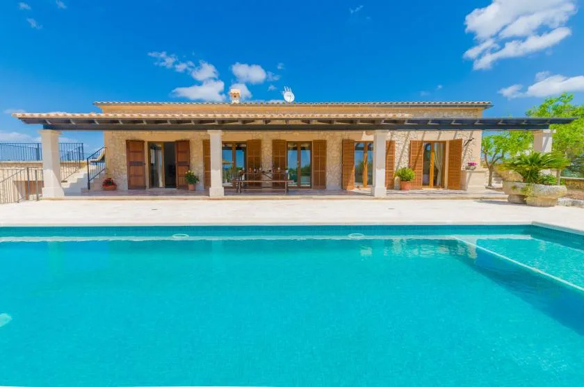 A swimming pool sits in front of a single-story building with a shaded patio.