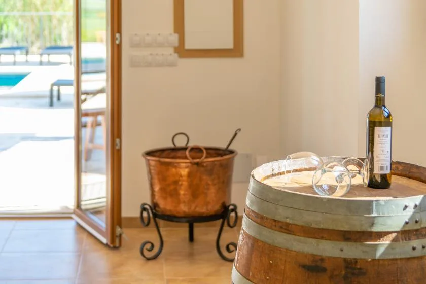 A wine bottle and glasses rest on a wooden barrel beside a copper tub.