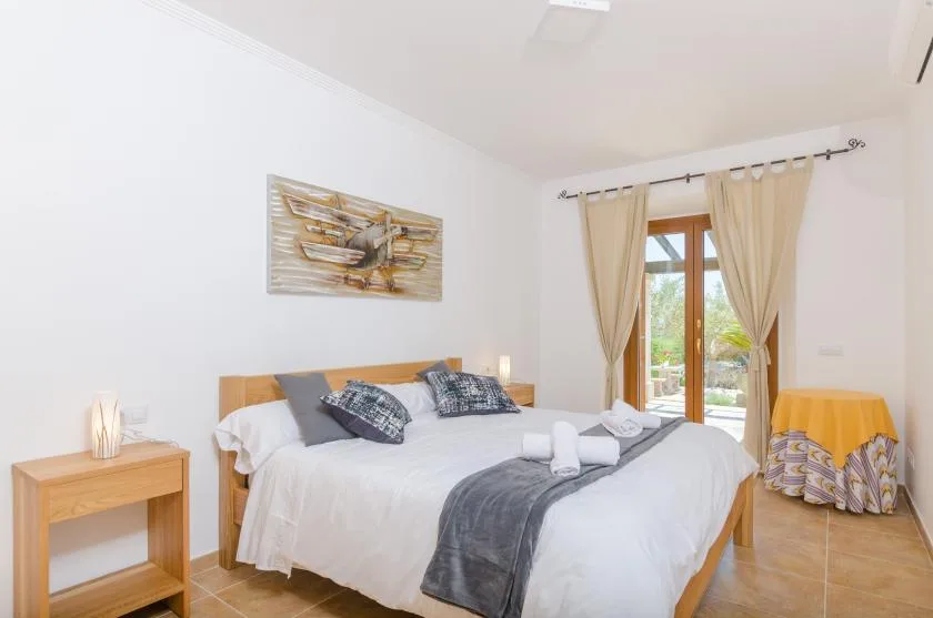 A bright bedroom with a double bed and curtains framing a glass door.