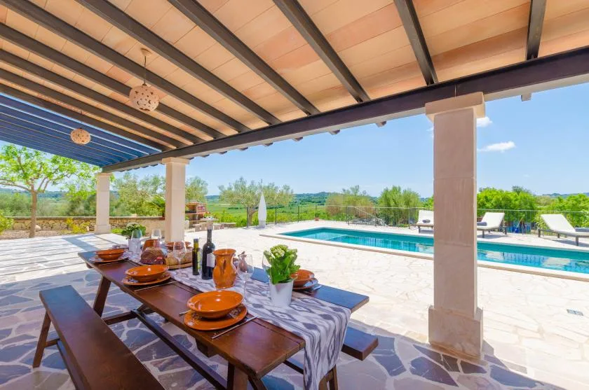 A covered outdoor dining area overlooks a swimming pool and open countryside.