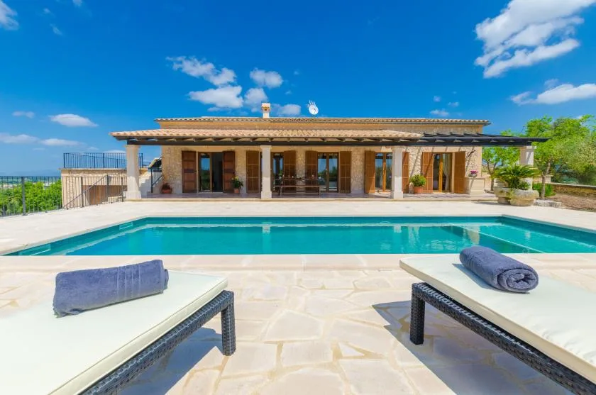 A swimming pool in front of a single-story building, with loungers nearby.