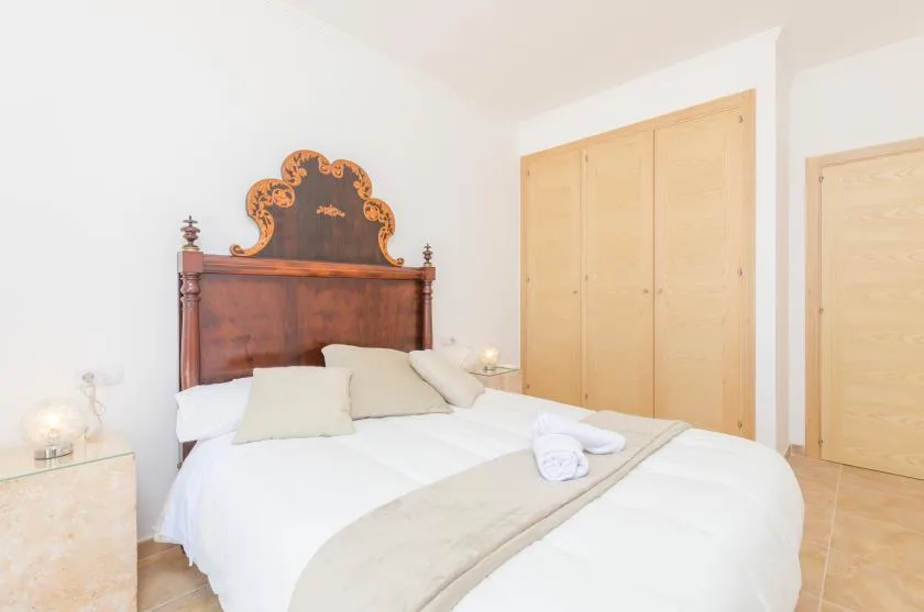 A bedroom with a large bed, wooden headboard, and light-colored bedding.