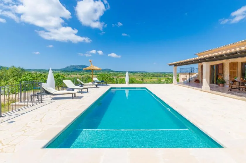 A swimming pool sits on a sunlit patio beside an open-sided pavilion.