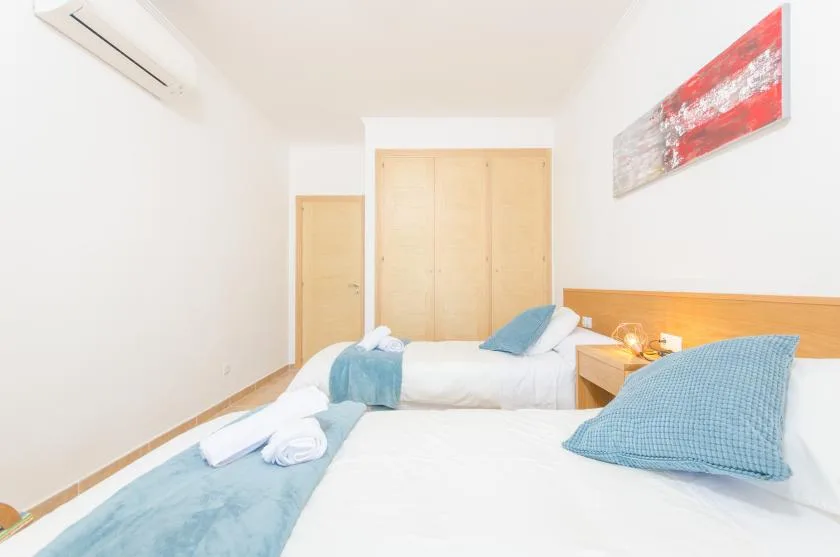A bright bedroom with beds, wooden wardrobes, and abstract wall art.