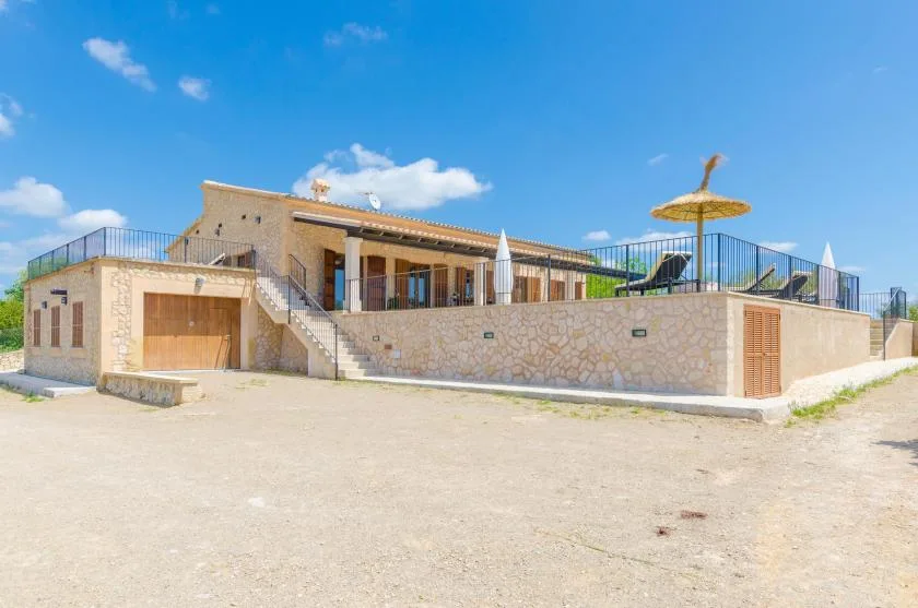 A stone house with a raised terrace, outdoor seating, and a thatched parasol.