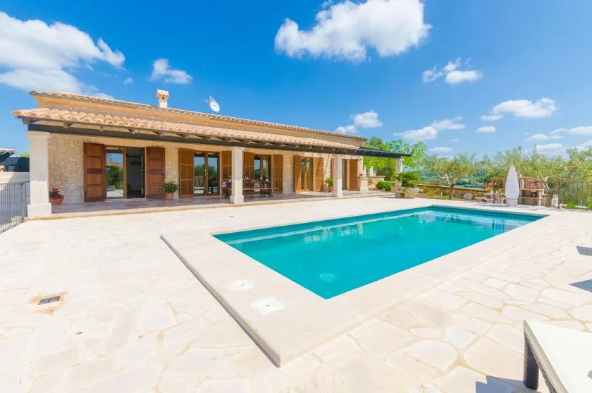 A swimming pool beside a single-story house, surrounded by a pale stone patio.
