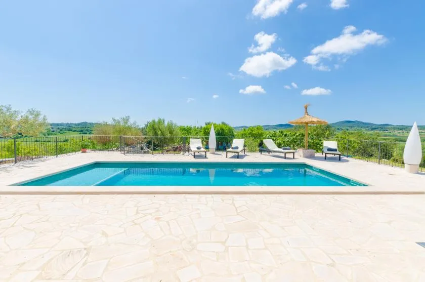 An outdoor swimming pool sits beside a spacious paved terrace with lounge seating.