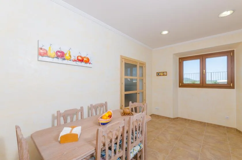 A dining area with a wooden table and chairs beneath a fruit painting.