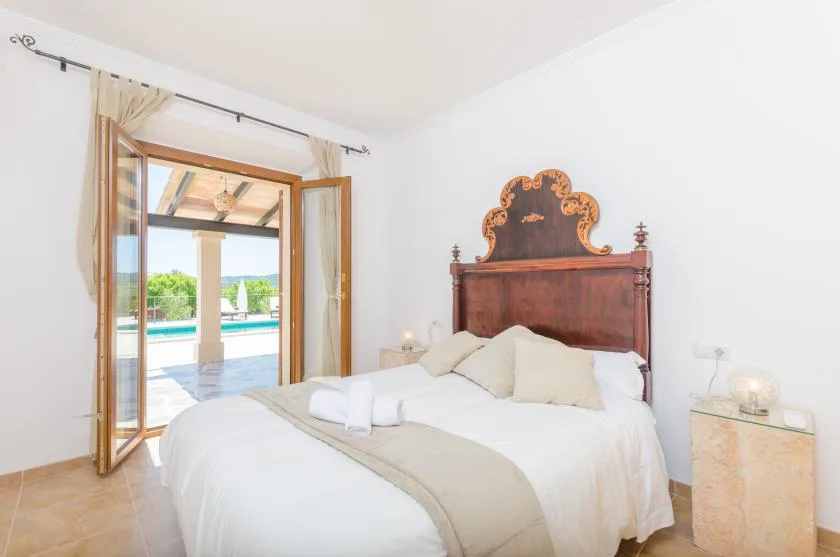 A bedroom with a neatly made bed and open doors overlooking a pool.