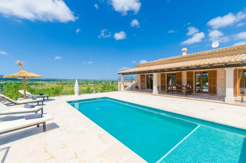 A sunny outdoor pool beside a tiled-roof house and lounge seating.