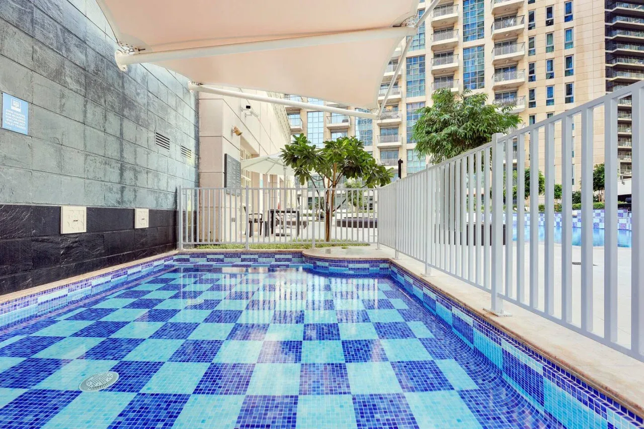 Una piscina al aire libre con suelo de azulejos azules bajo un toldo.