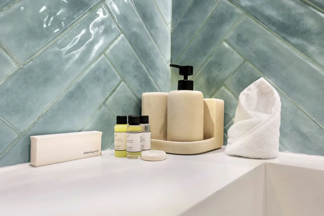 Encimera de baño con artículos de aseo y una toalla doblada junto a una pared de azulejos.