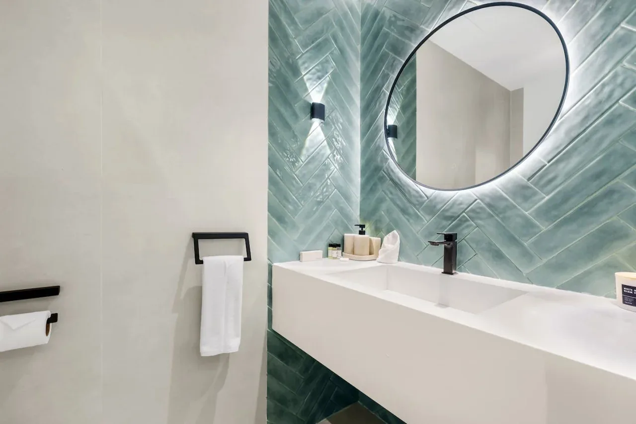 Un tocador de baño moderno con espejo ovalado y pared de azulejos verdes.