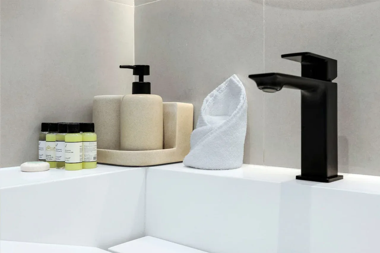 Un lavabo de baño con grifo negro, dispensador de jabón y toalla doblada.