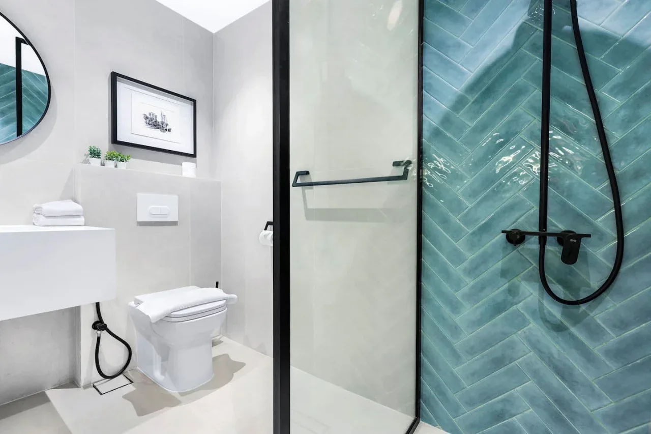 Un baño moderno con lavabo blanco, inodoro y ducha con azulejos azules.