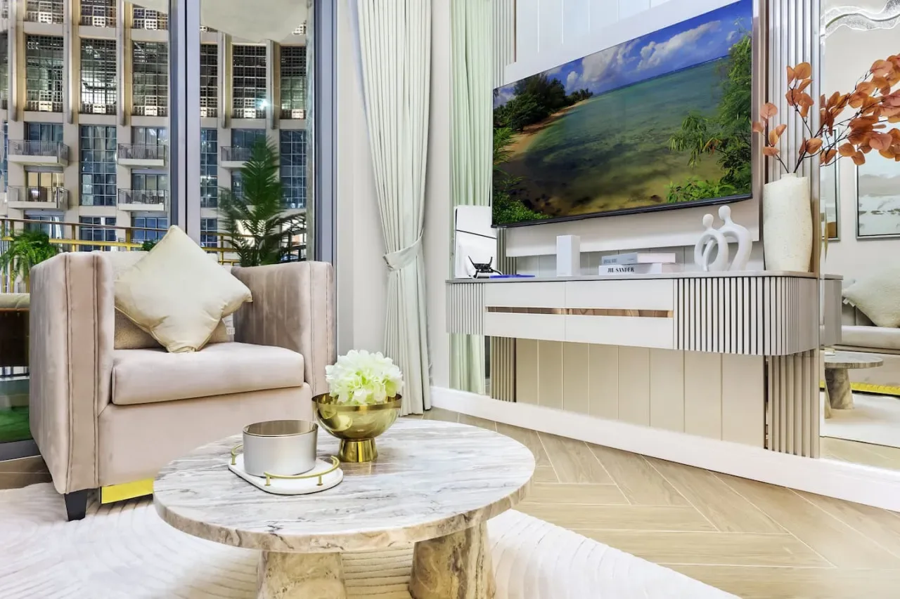 Una sala luminosa con un asiento acolchado, una mesa de centro redonda y un televisor.