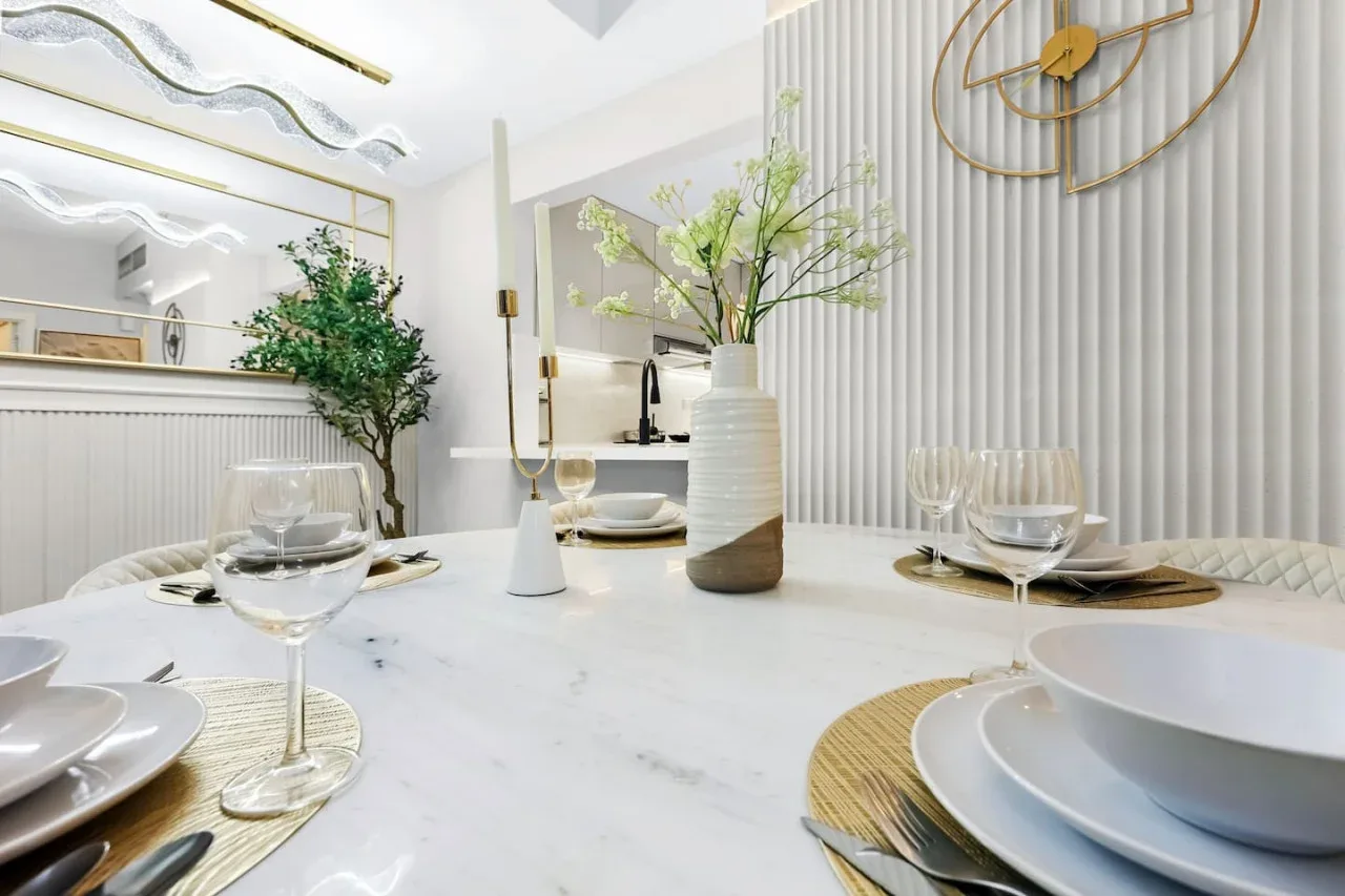 Un comedor luminoso con una mesa puesta con vajilla y un jarrón con ramas.