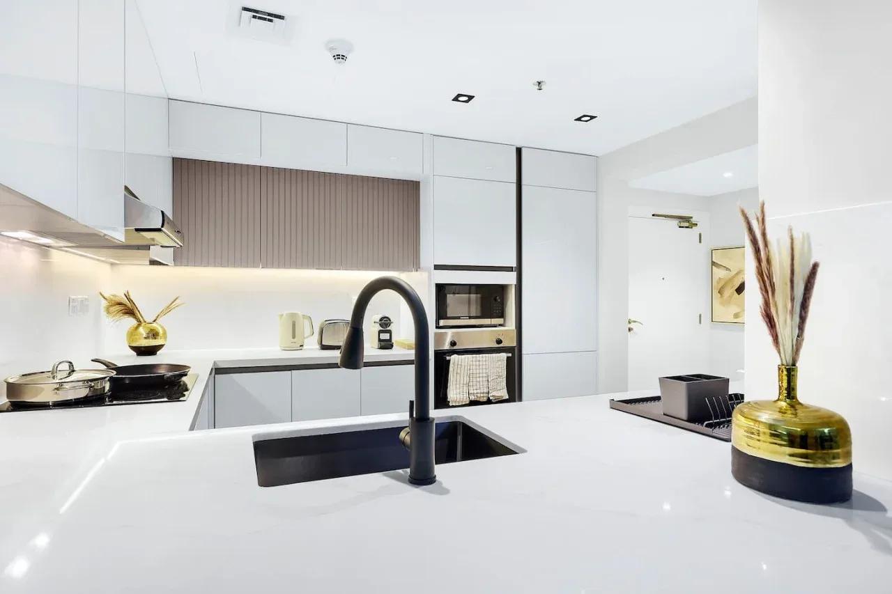 Una cocina moderna y luminosa con una gran isla blanca y un grifo oscuro.