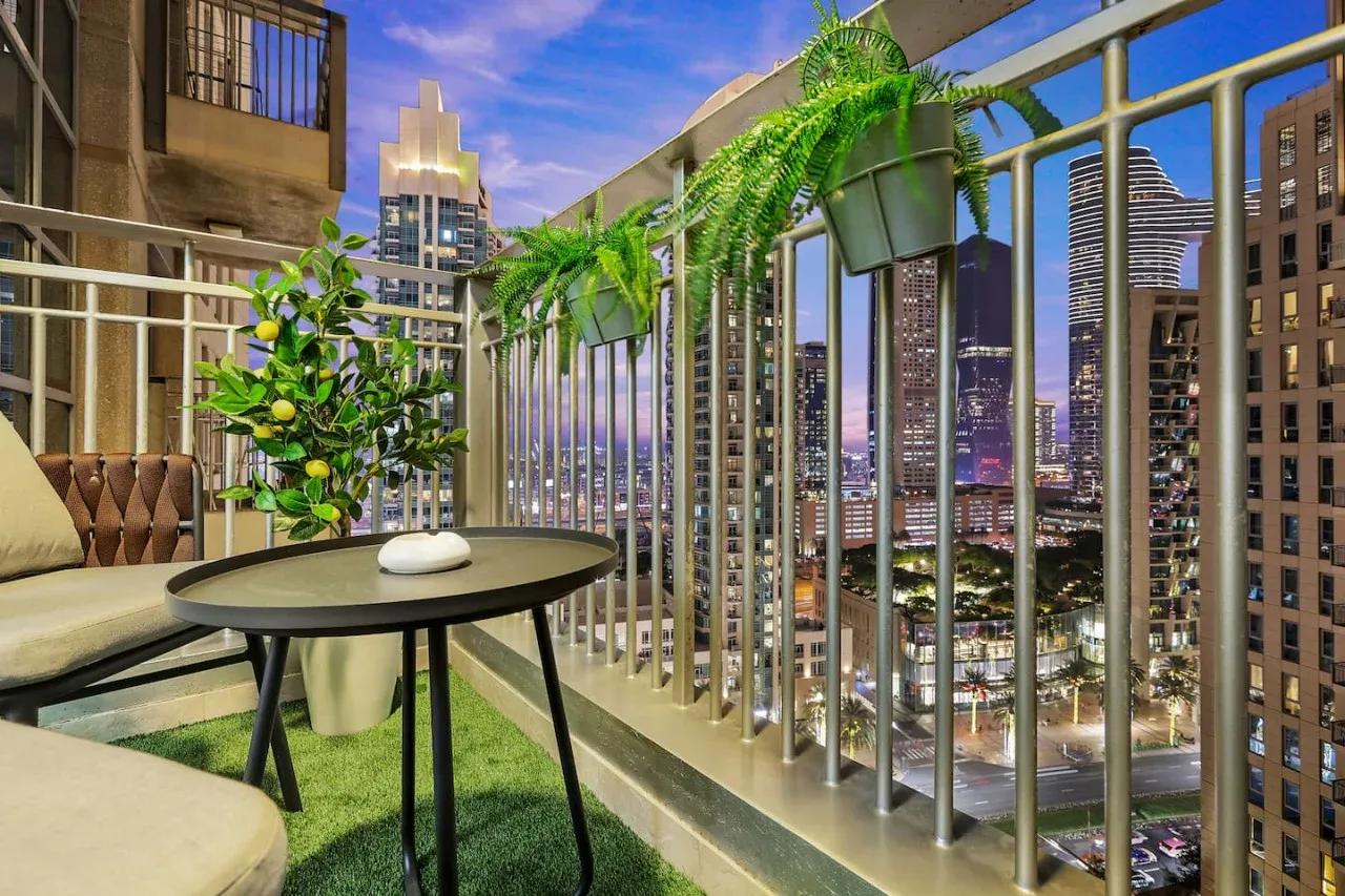 Una zona de estar en un balcón con plantas en macetas da a un horizonte urbano.
