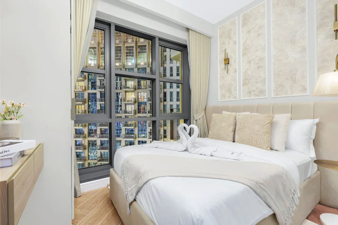 Un dormitorio luminoso con una cama bien tendida junto a grandes ventanas.