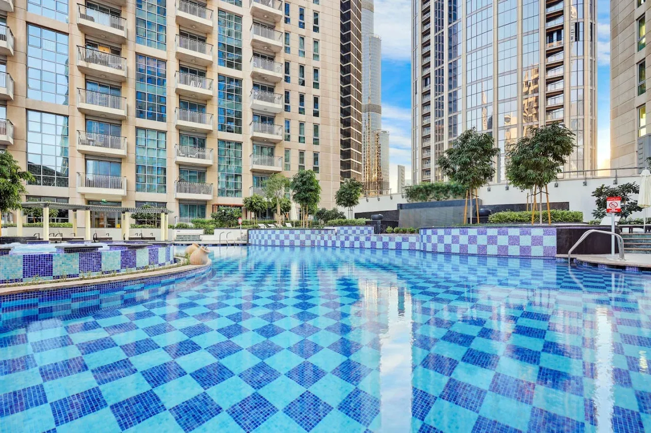 Una piscina al aire libre con suelo de azulejos azules está rodeada de edificios residenciales altos.