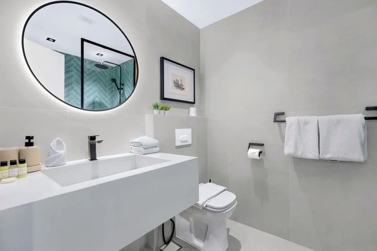 Un baño luminoso con lavabo, inodoro y ducha reflejada en el espejo.