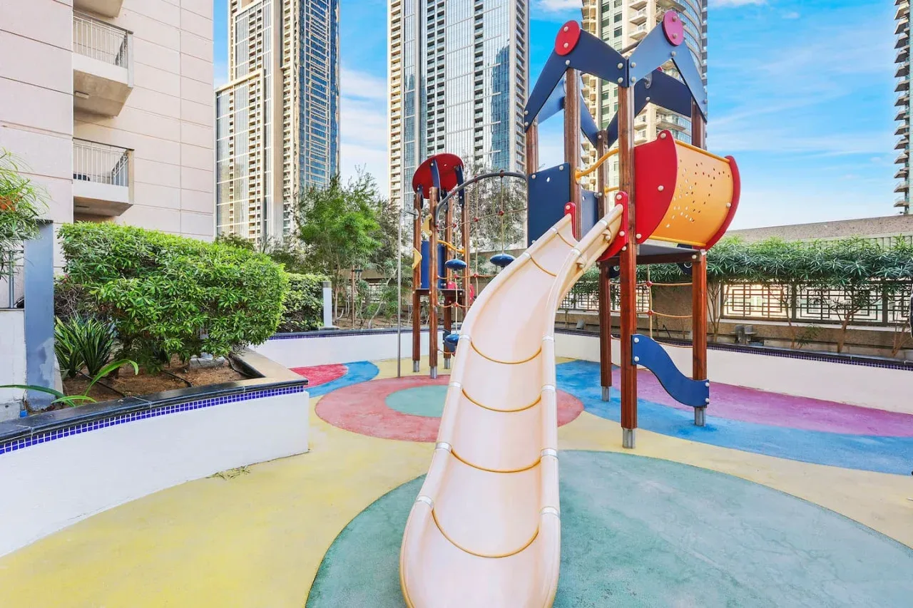 Un parque infantil colorido al aire libre con toboganes y estructuras para trepar entre edificios altos.