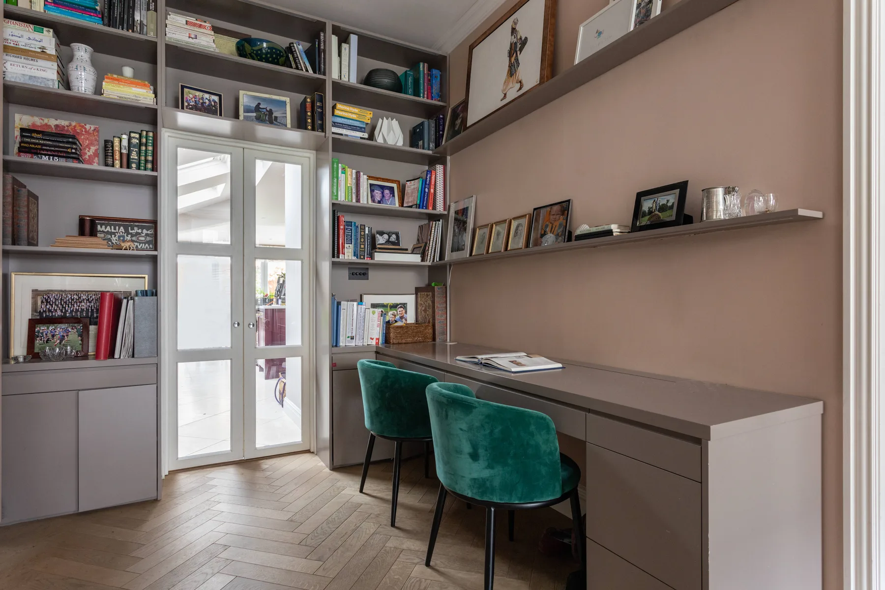 A home office with a long desk, green seating, and built-in shelves.