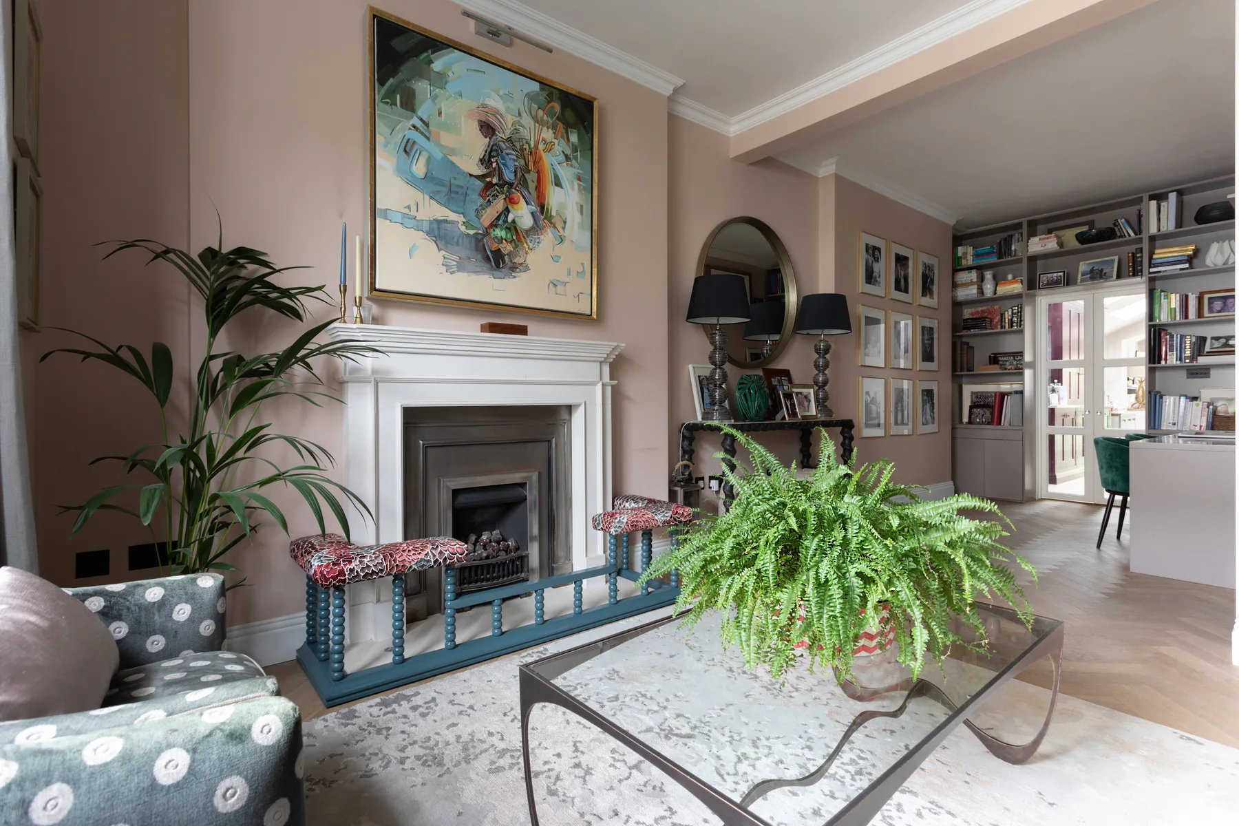 Una sala de estar con chimenea, una obra enmarcada y una gran planta frondosa.