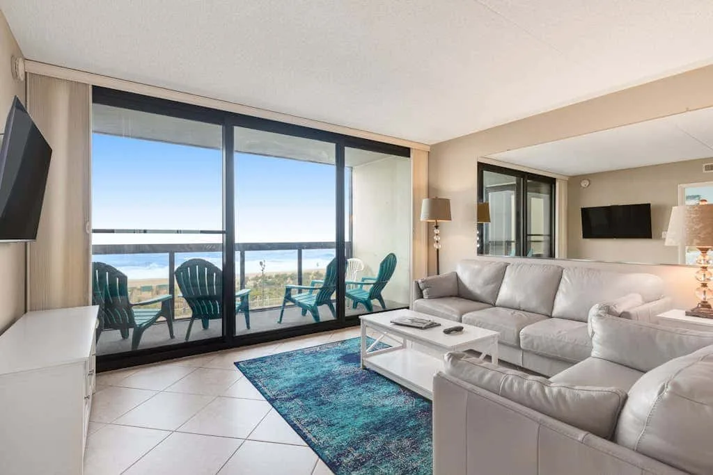 A living room with a sectional sofa, coffee table, and large windows overlooking the water.