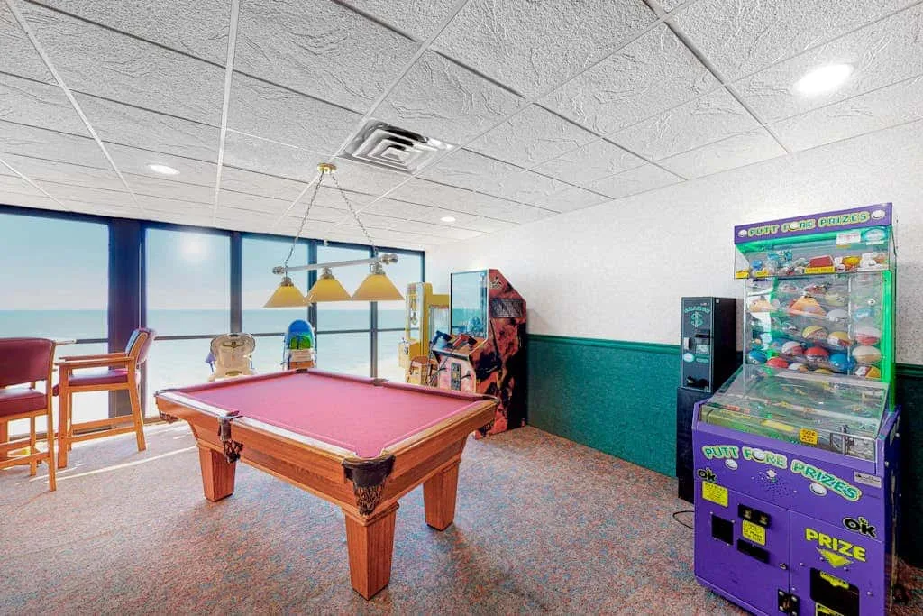 A game room with a pool table, vending machine, and large windows.
