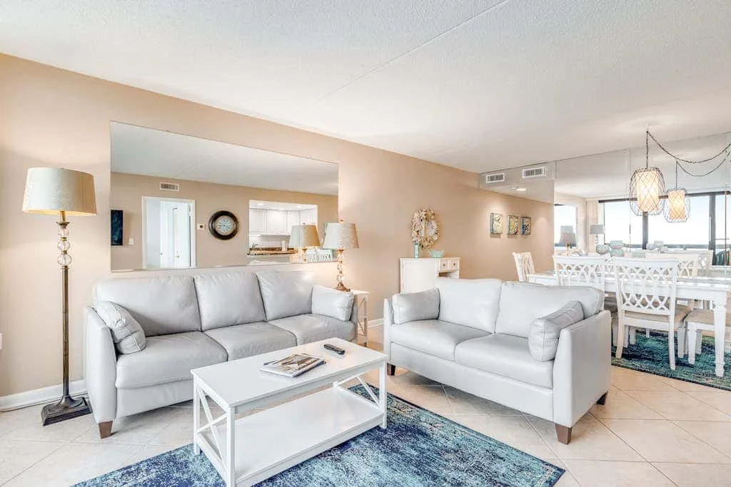 A bright living room with light seating, a coffee table, and a dining area.