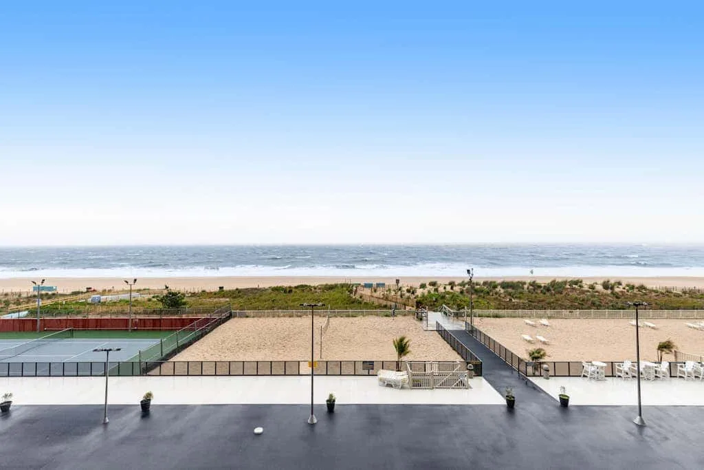 A beachfront view shows a sandy shore, ocean, and outdoor tennis courts.
