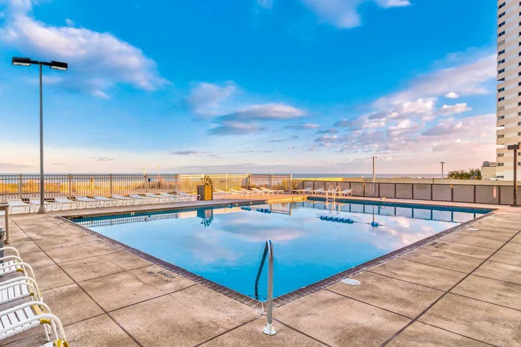 An outdoor swimming pool sits on a paved deck beside a railing.