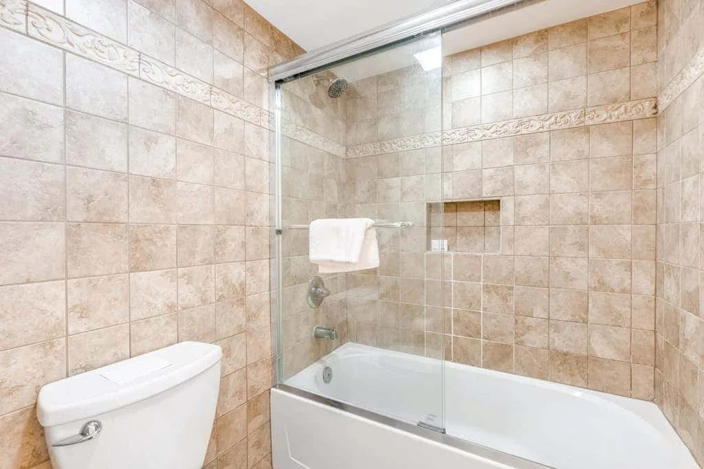 A tiled bathroom with a bathtub and glass shower screen.