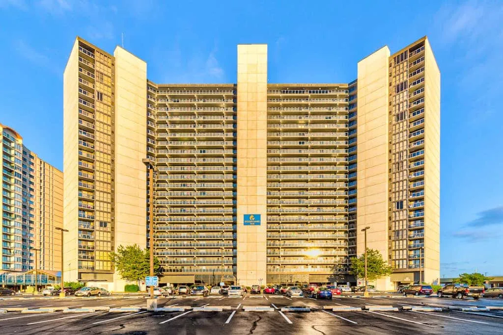 A tall apartment building overlooks a parking lot under a clear blue sky.
