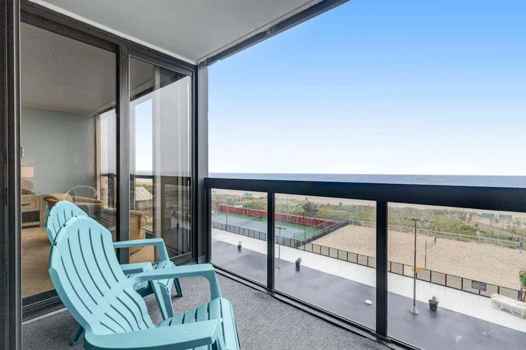 A balcony with blue seating overlooks a paved outdoor area and distant fields.
