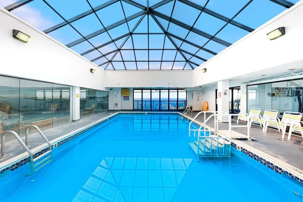 An indoor swimming pool beneath a glass roof, with seating along the side.