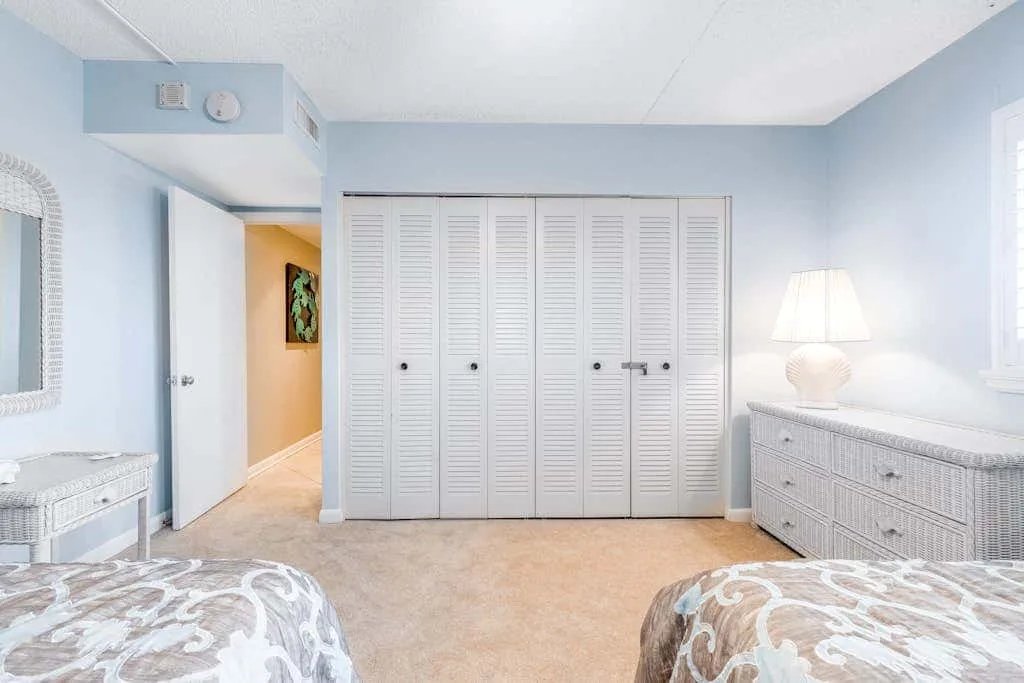 A bright bedroom with louvered closet doors and two beds.