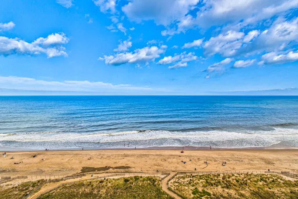 A sandy beach borders the blue sea beneath a partly cloudy sky.