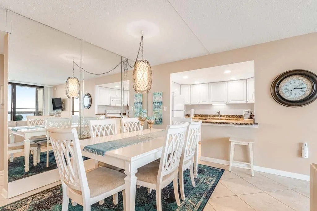 A dining area with white tables and chairs beside an open kitchen.
