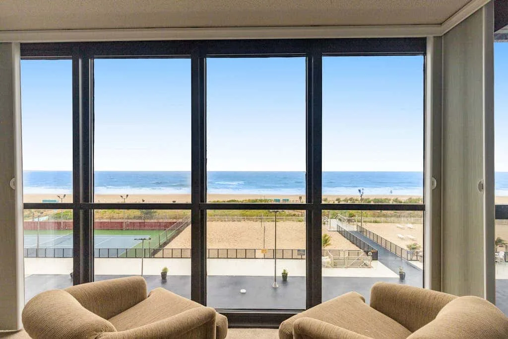 A living area with seating faces the beach and ocean through large windows.