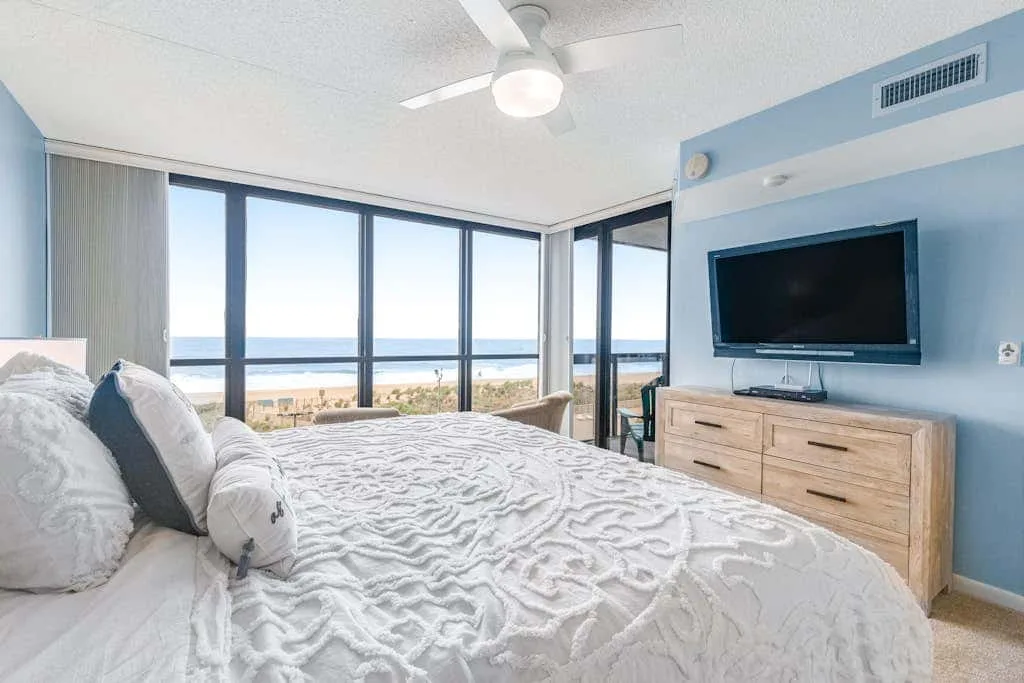 A bright bedroom with a large bed facing windows overlooking the water.