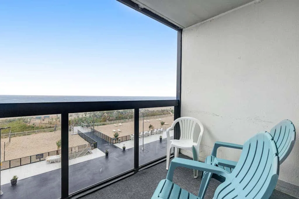 A covered balcony overlooks the sea, with plastic seating beside the railing.