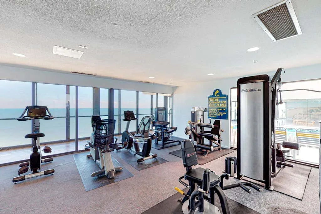 A fitness room with exercise machines beside large windows overlooking the water.