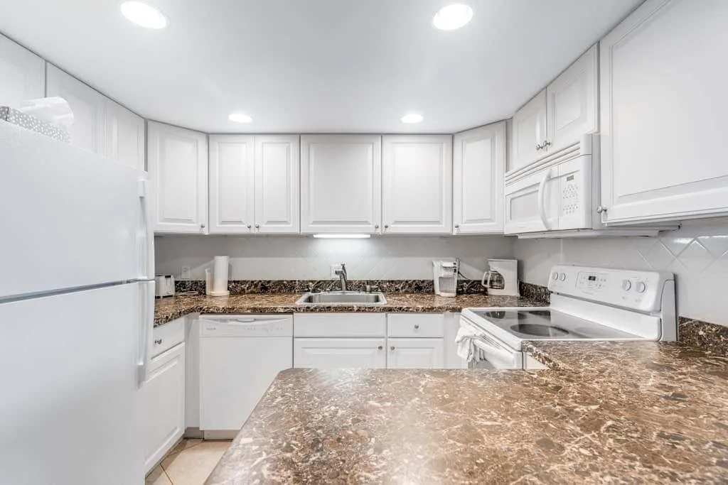 A bright kitchen with white cabinets and brown countertops.