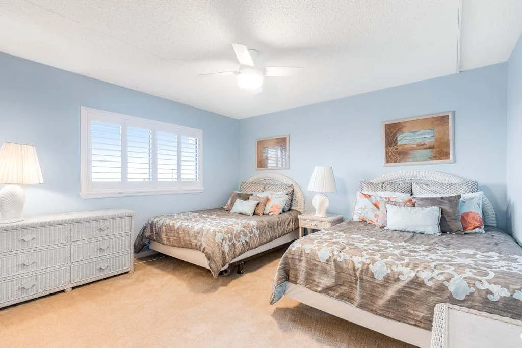 A bedroom with two beds and a window with white shutters.